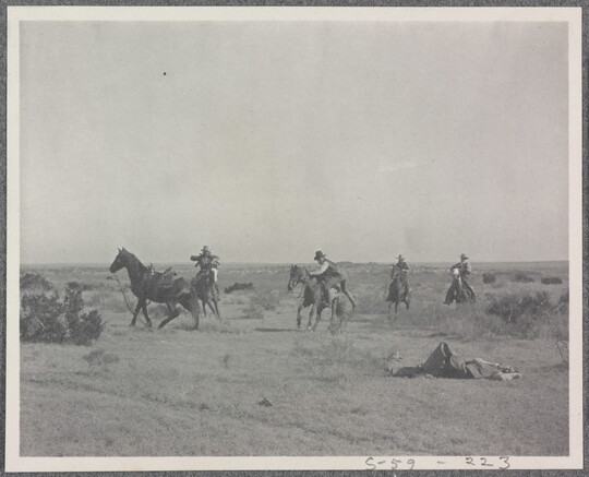 A black-and-white photograph of a group of men on horseback and one man lying on the ground.