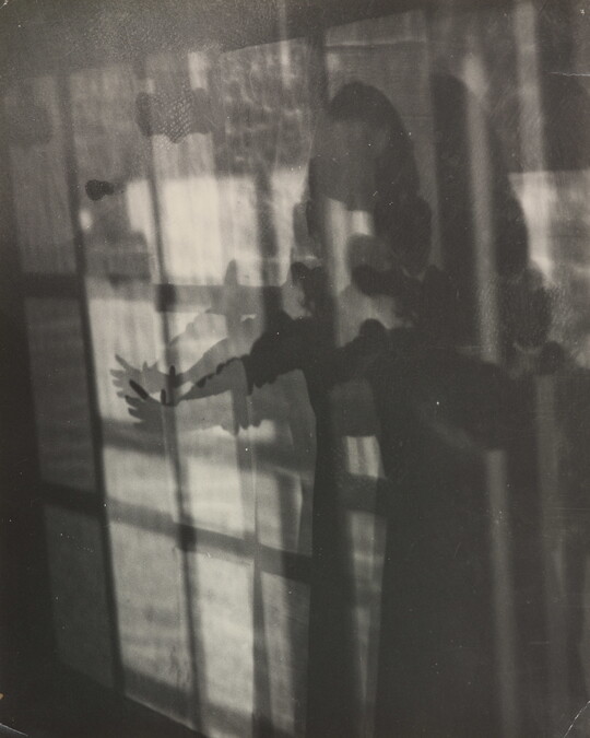 An abstract black-and-white photograph showing a human figure extending their arm in abstracted layers of shadow and light.