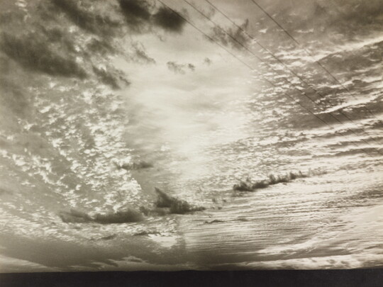 A black-and-white photograph of sunlight shining through layers of clouds.