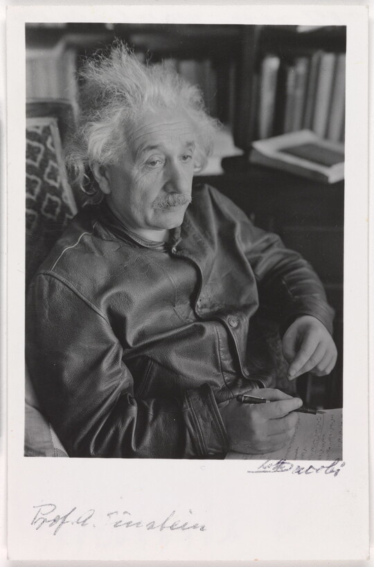 A black-and-white photograph of a seated older White man with wild white hair and mustache above handwritten notes.