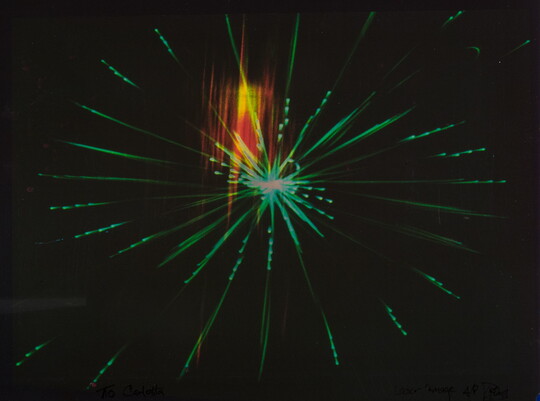 An abstract color photograph of a bright green starburst with a rectangle of orange and yellow light on a black background.