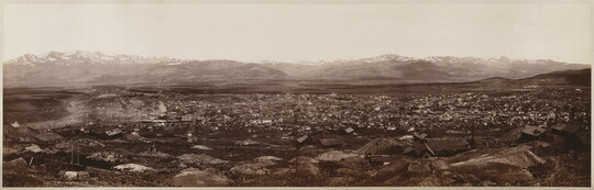 A black-and-white panoramic landscape photograph of a city with a mountain range in the background.