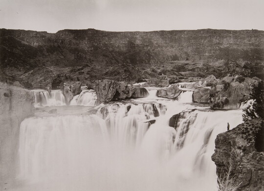 A black-and-white photograph of a wide, rocky waterfall.