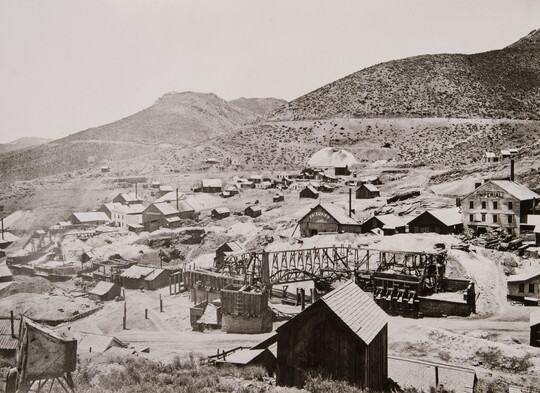 A black-and-white photograph of a mining town at the base of mountains.