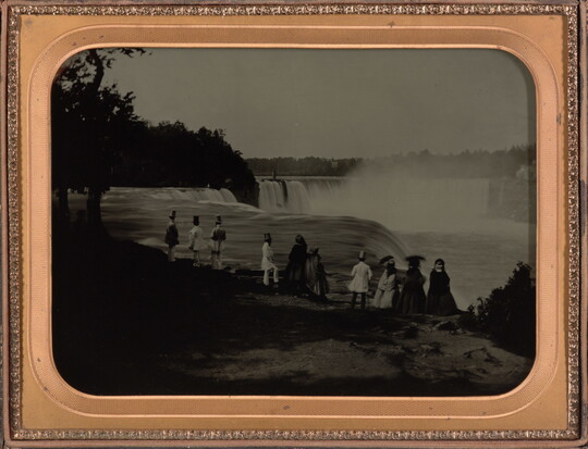 A black-and-white photograph in a gold frame of a group of men and women on a cliff overlooking a large waterfall.