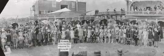 A black-and-white panoramic photograph of a large group of women in different 1920s-style bathing suits, some with parasols.