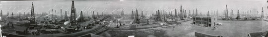 A black-and-white panoramic photograph of a massive oil field filled with wells and factory buildings.