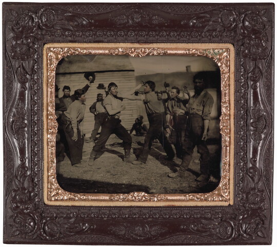 A framed black-and-white photograph of two men pretending to fight surrounded by other men who are watching.