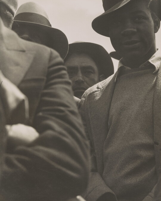 A black-and-white photograph of a close-up of a group of men wearing hats, sweaters, and jackets.