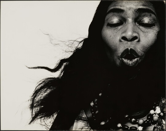 A black-and-white close-up photograph of a Black woman singing with her eyes closed.