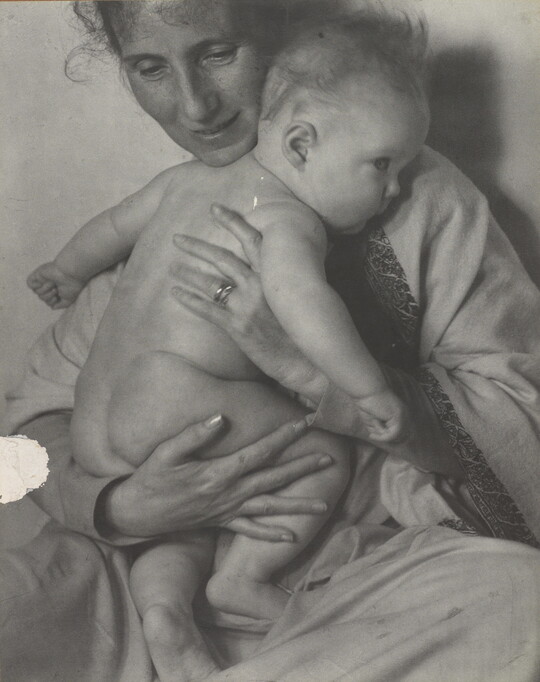 A black-and-white photograph of a White woman holding a naked baby to her chest.