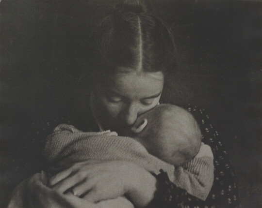 A black-and-white photograph of a White woman holding an infant to her chest while she rests her cheek on the infant's cheek.