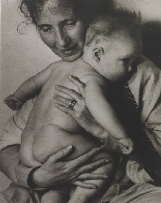 A black-and-white photograph of a White woman holding a naked baby to her chest.