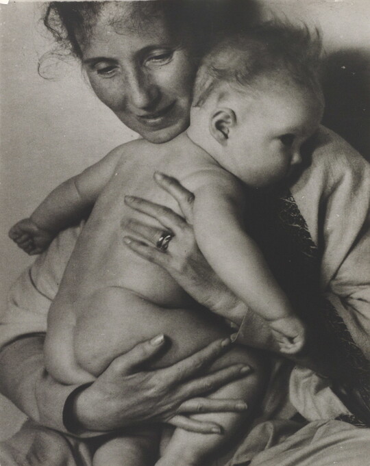 A black-and-white photograph of a White woman holding a naked baby to her chest.