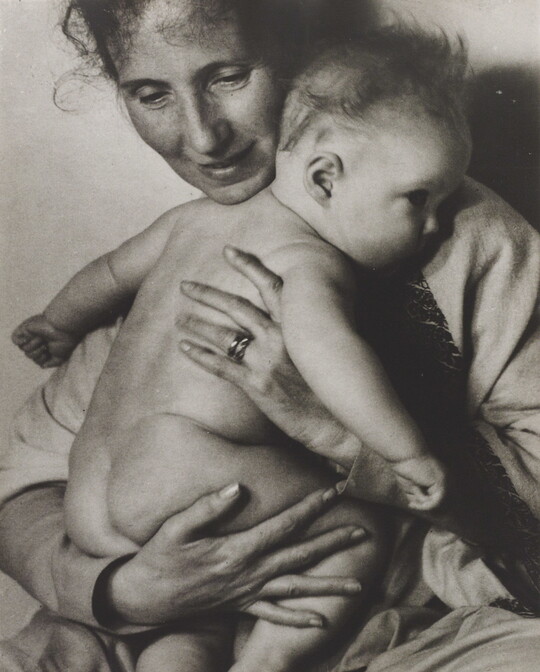 A black-and-white photograph of a White woman holding a naked baby to her chest.