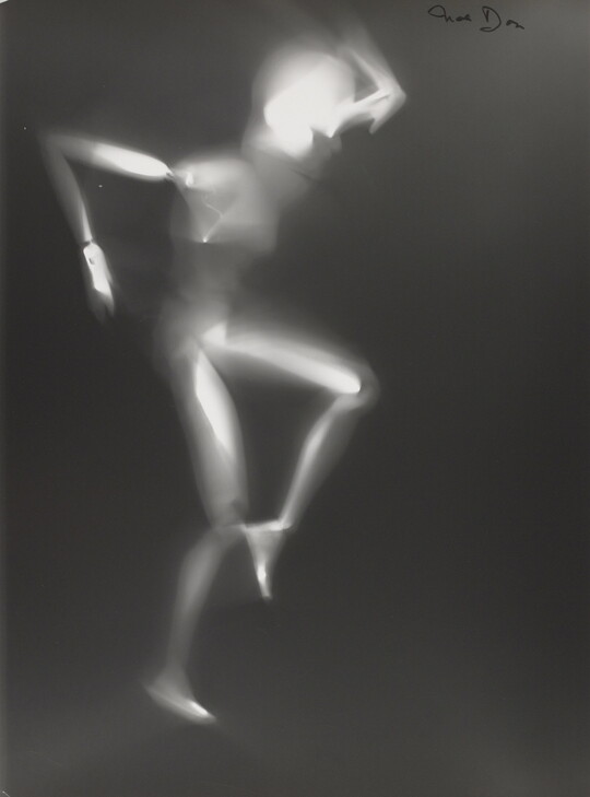 A black-and-white photograph of a white person-shaped puppet dancing on a black background.