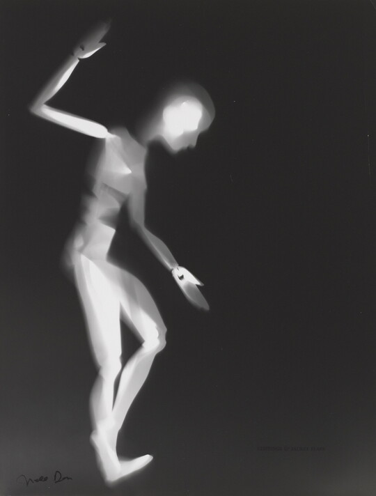 A black-and-white photograph of a white person-shaped puppet dancing on a black background.