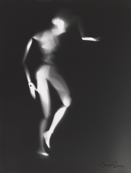 A black-and-white photograph of a white person-shaped puppet dancing on a black background.