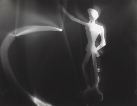 An abstract black-and-white photograph of an illuminated white figure and blurred lights against a black background.