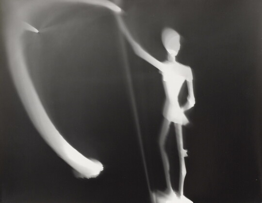 An abstract black-and-white photograph of an illuminated white figure and blurred lights against a black background.