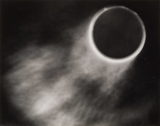 An abstract black-and-white photograph of what looks like a solar eclipse with light fanning out from the circles.