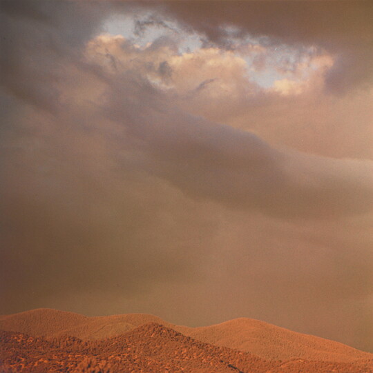 A color photograph of reddish mountaintops under dark, heavy clouds.
