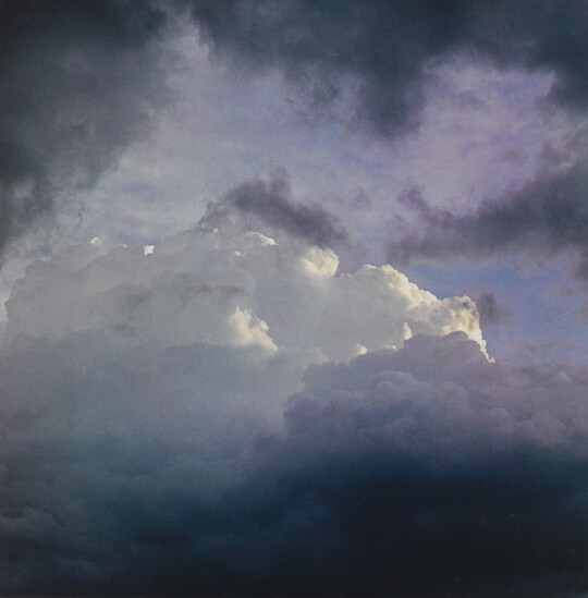 A color photograph of dark clouds framing brighter, fluffy clouds in the center.