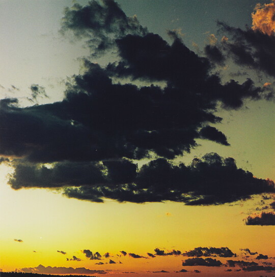 A color photograph of dark clouds in a sky of orange, yellow, blue, and gray.