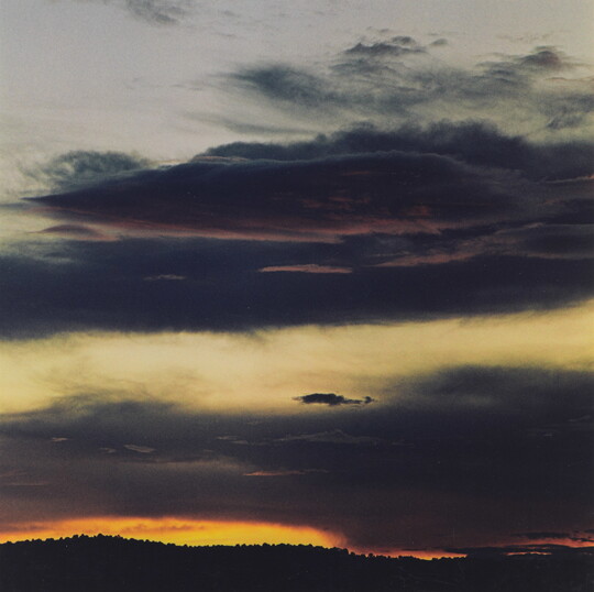 A color photograph of dark clouds in the sky and the sun setting at the horizon.
