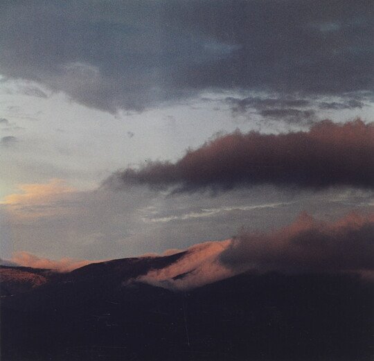 A color photograph of a mountain range with clouds in a blue and pink sky.