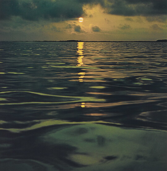 A color photograph of a sunset reflected over a calm, dark ocean.