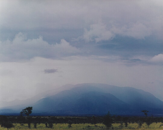 A color photograph of a purple and blue mountain range veiled in fog and clouds.