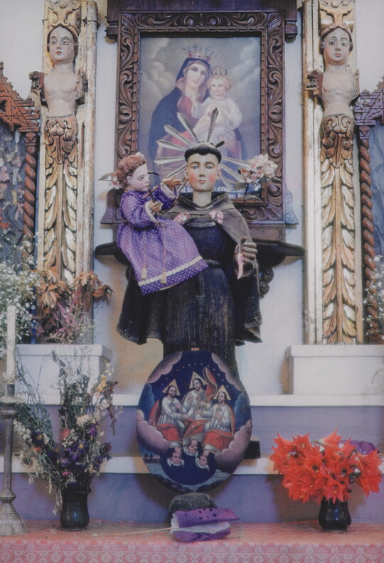 A color photograph of a decorative church altar with a statue of a saint holding a baby Christ figure in a purple robe.