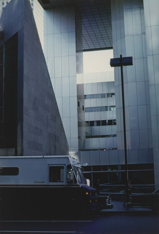 A color photograph of a delivery van parked in front of a modern skyscraper.