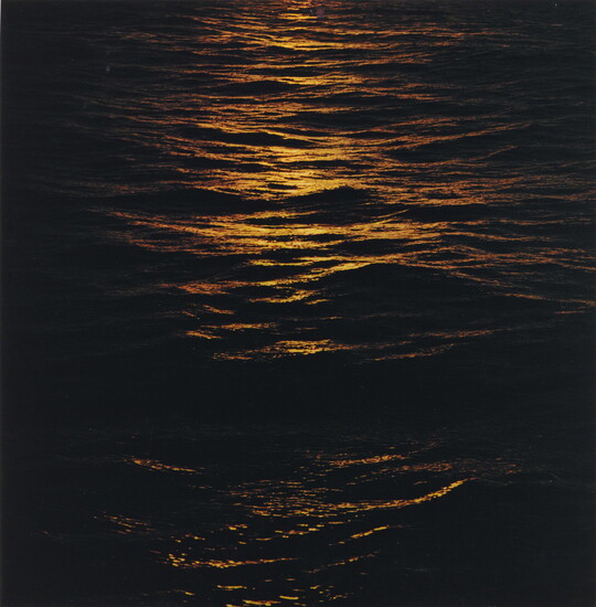 A color photograph of dark ocean waves at night reflecting orange light on the tops of the waves.