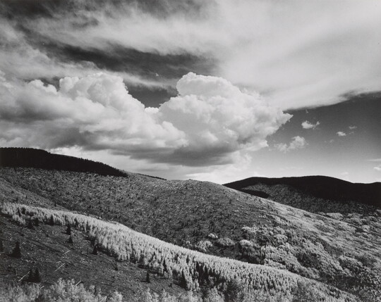 A black-and-white landscape photograph of a mountainous terrain under a partly cloudy sky.