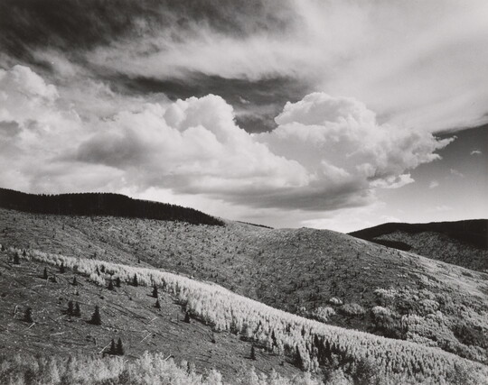 A black-and-white landscape photograph of a mountainous terrain under a partly cloudy sky.