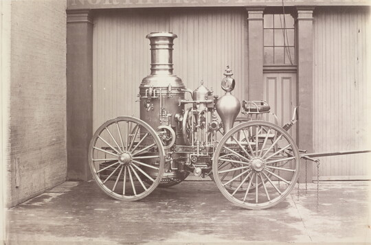 A black-and-white photograph of a parked wagon with a large tank and other mechanical features.