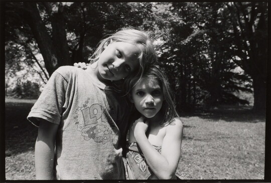 A black-and-white photograph of two young White girls, the taller one resting her head on the head of the other.