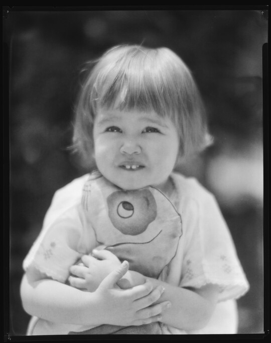 A black-and-white image of a young White child with short hair hugging a stuffed toy.