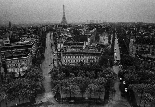 A black-and-white photograph taken from above of city streets fanning out toward the Eiffel Tower in the distance.