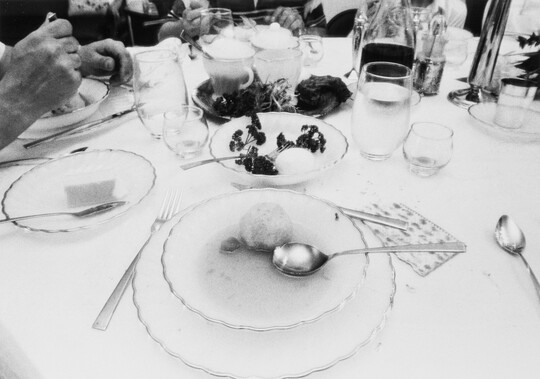 A black-and-white photograph of a place setting of a bowl of soup surrounded by dishes, glasses, and silverware.