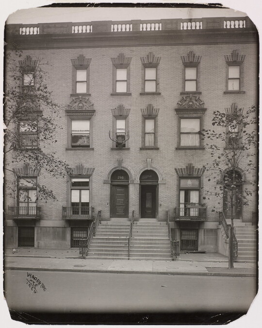 A black-and-white photograph of the facades of three-story row homes with steps leading to front doors.