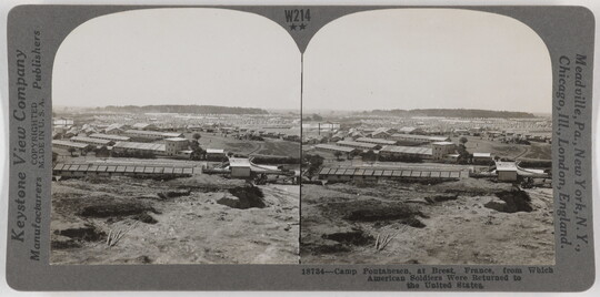 Two almost identical side-by-side black-and-white photographs of a mostly flat landscape with a few trees and long, flat industrial buildings.