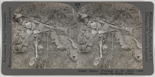 Two almost identical side-by-side black-and-white photographs of a human skeleton laying in the dirt amongst remnants of clothing and weapons.