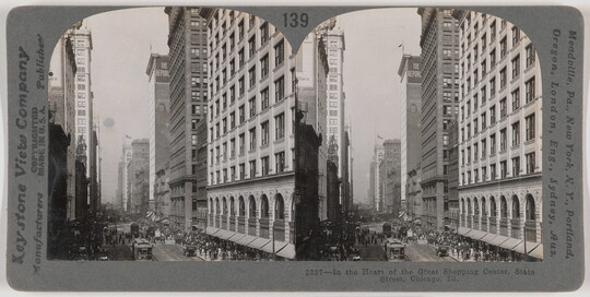 Two almost identical side-by-side black-and-white photographs of tall city buildings next to a busy street with pedestrians and streetcars.