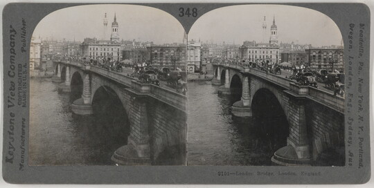 Two almost identical black-and-white photographs side by side of a brick arch bridge that spans a river, pedestrians and cars on top, and a city skyline in the background.