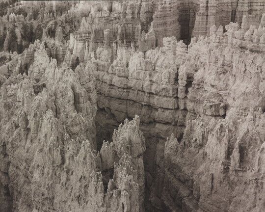 A black-and-white landscape photograph of a view of banded rock formations in a canyon.
