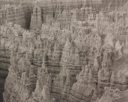 A black-and-white landscape photograph of a view of banded rock formations in a canyon.