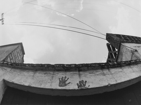 A black-and-white photograph looking up at a concrete lintel that has two distinct handprints on it.